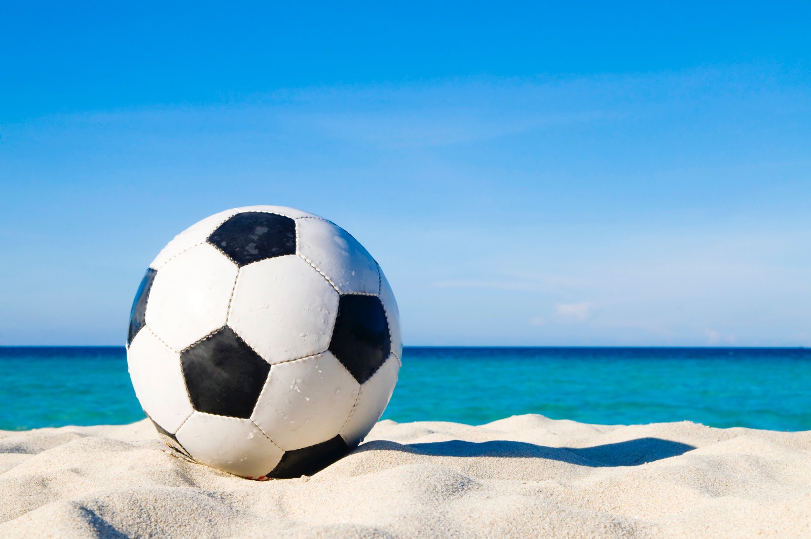 Uma bola de futebol na praia com água azul ao fundo (praia, bola, futebol, bola de futebol, azul celeste)