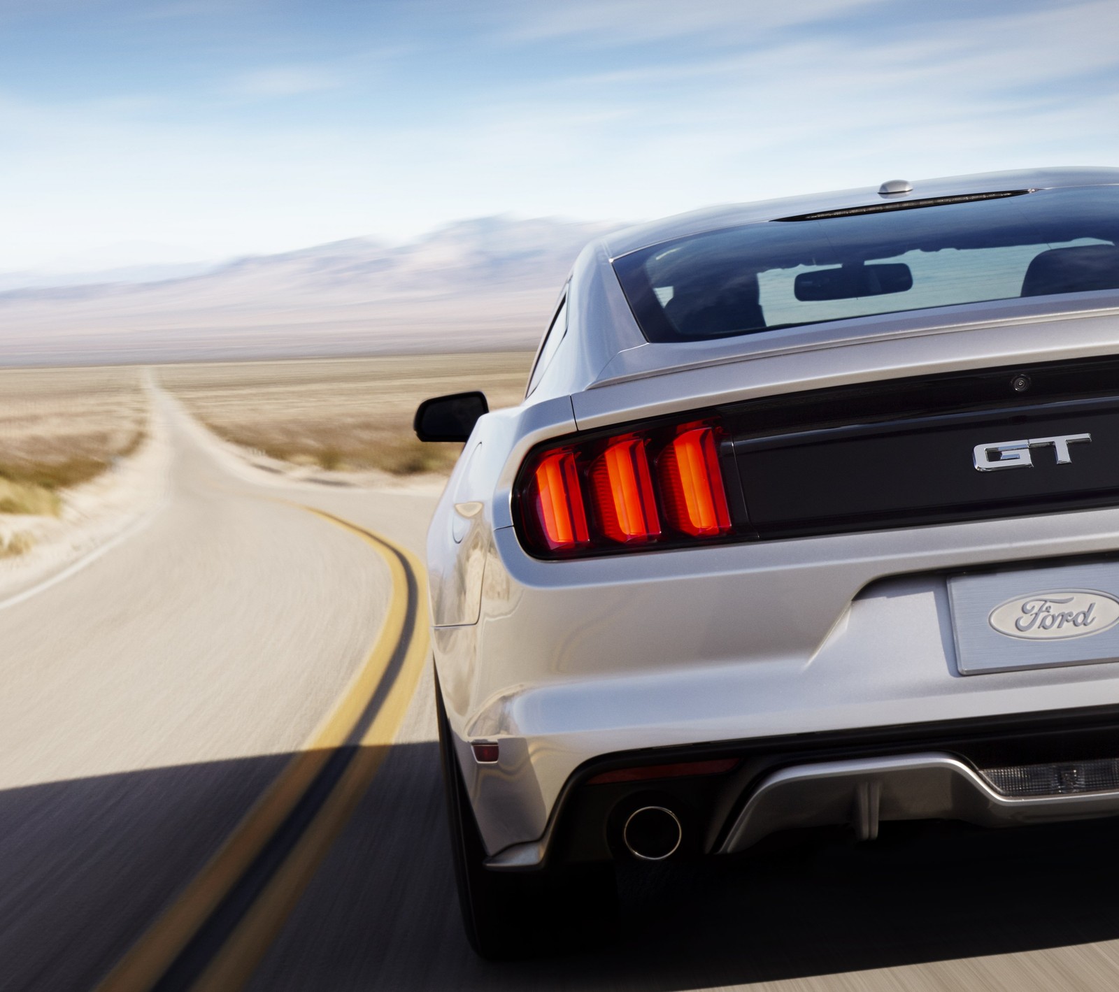 A close up of a silver mustang driving down a road (car, ford, muscle, road)