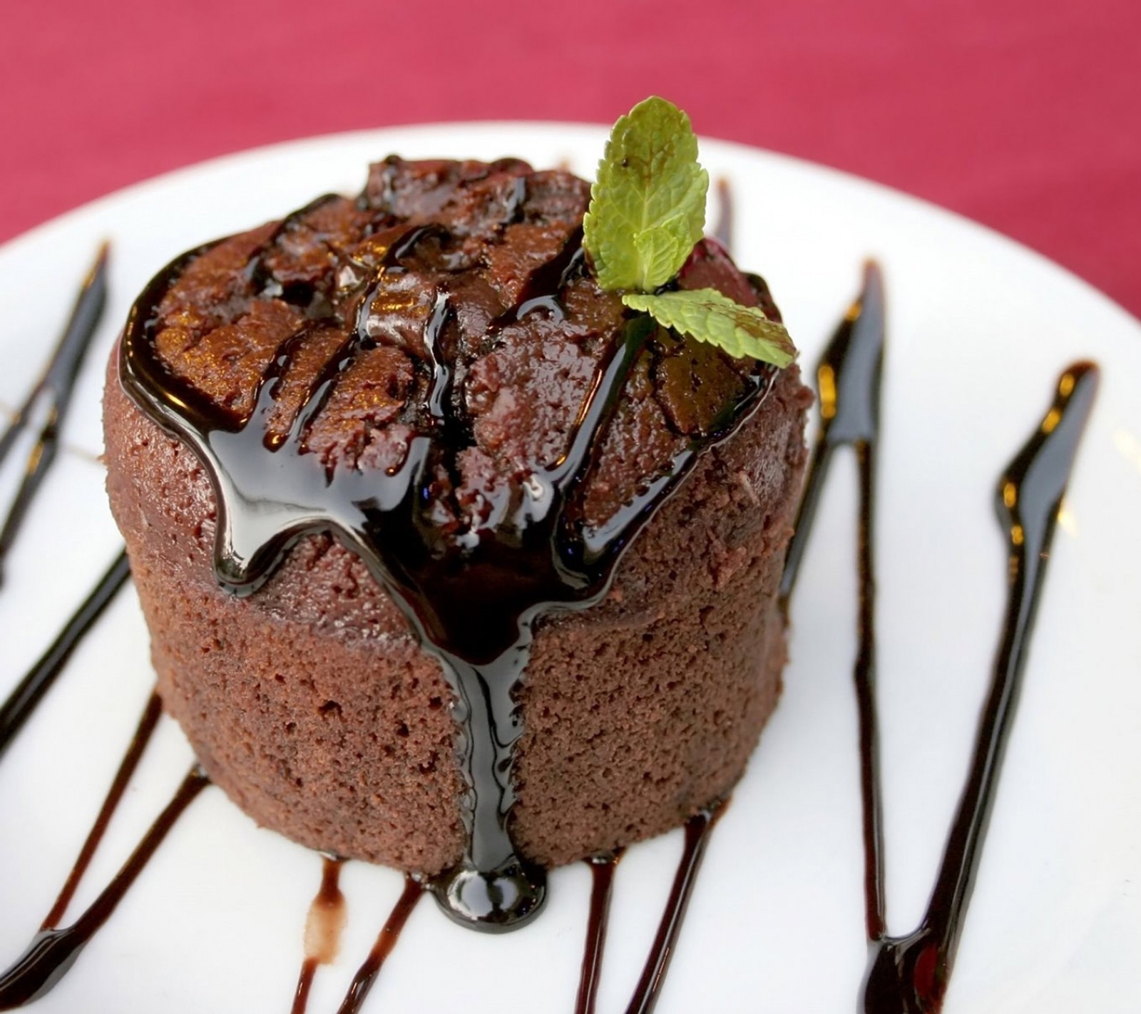 Hay un pastel de chocolate con salsa de chocolate y una hoja de menta encima (negro, marrón, pastel, chocolate, pastelito)