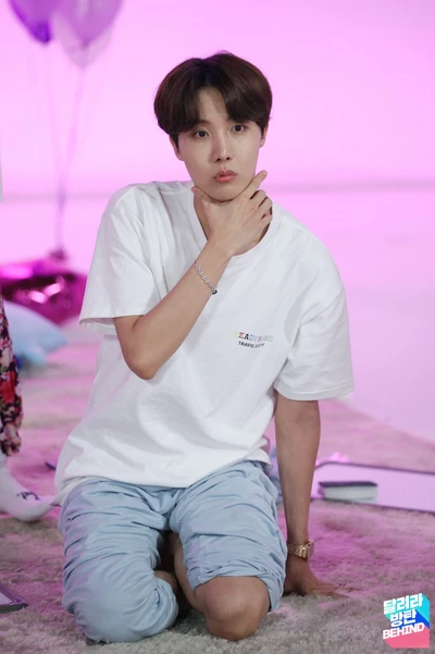 J-Hope de BTS posando pensativo en un atuendo casual contra un fondo rosa vibrante.