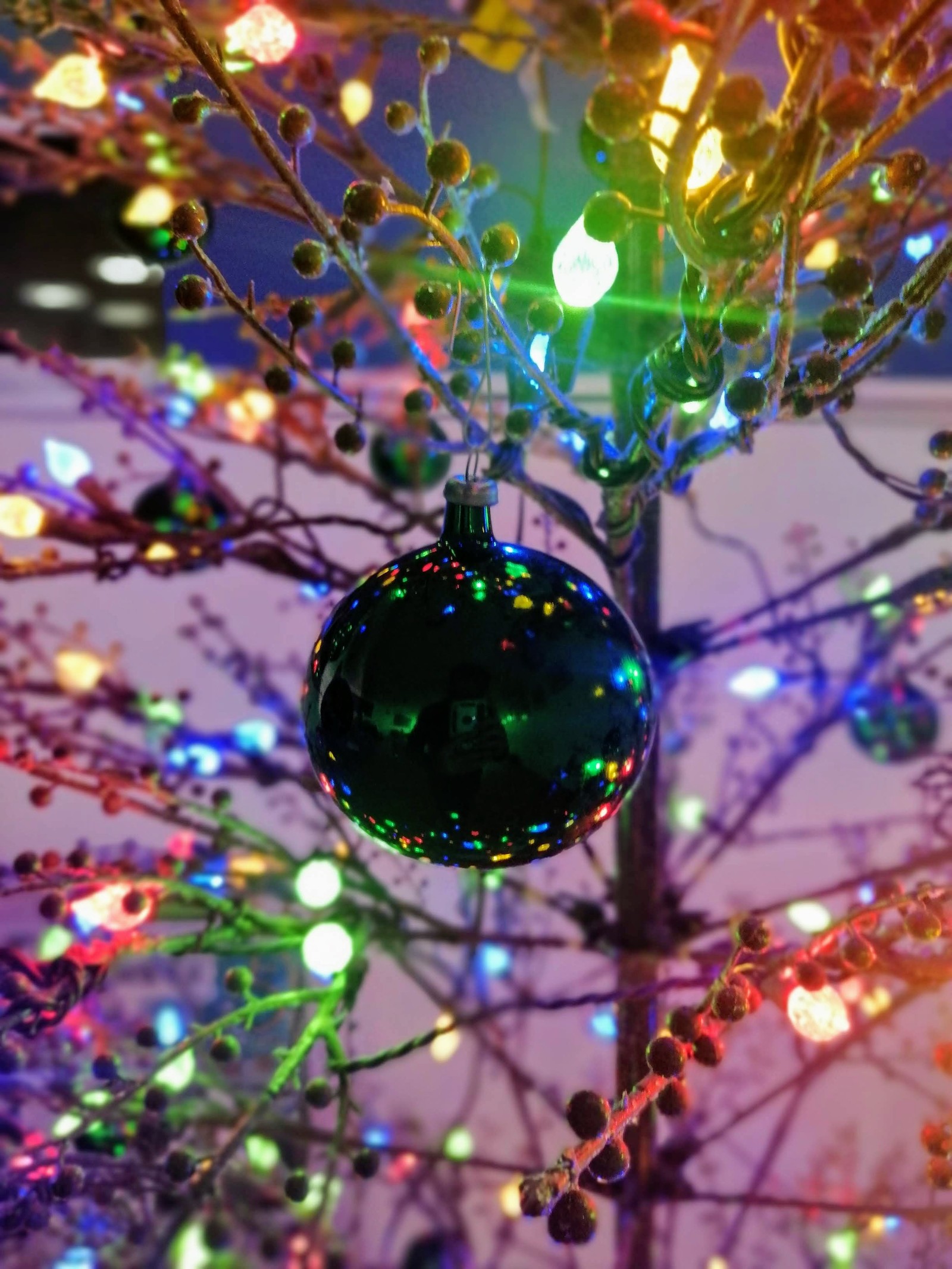 There is a christmas tree with a colorful ornament hanging from it (arbol, ball, esfera, luces, navidad)