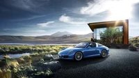 Porsche 911 Targa bleu garé à côté d'une maison architecturale moderne avec un paysage pittoresque en arrière-plan.