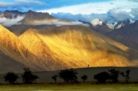 Majestuosa cordillera montañosa al amanecer: una figura solitaria en medio de tierras altas doradas y un cielo dramático.