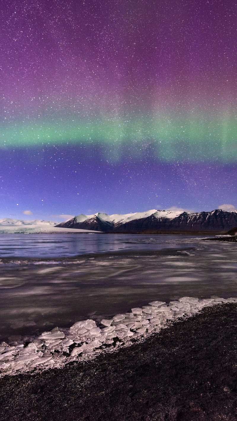 Luzes auroras roxas e verdes sobre um corpo d'água com montanhas ao fundo (aurora, geleira, luz, água, paisagem natural)