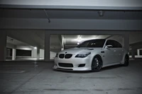 Sleek white BMW M5 parked in a dimly lit garage, showcasing its sporty design and modern luxury.