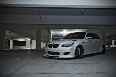 Elegante BMW M5 branco estacionado em uma garagem mal iluminada, exibindo seu design esportivo e luxo moderno.