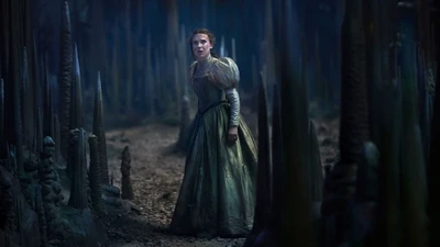 A young woman in a flowing green gown stands in a dark, enchanted forest, surrounded by tall, jagged formations.