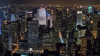 Illuminated Manhattan skyline at night, showcasing a vibrant urban landscape filled with towering skyscrapers against a sprawling city horizon.