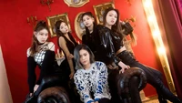 Membros do ITZY em trajes pretos elegantes contra um fundo vermelho ousado