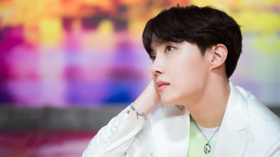 J-Hope of BTS in a contemplative pose against a colorful background.