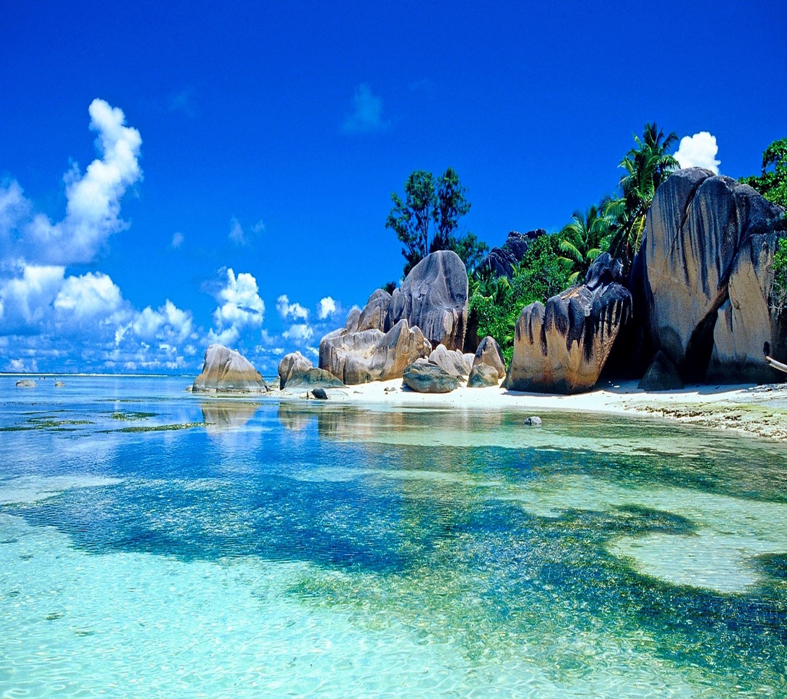 There is a large rock formation on the beach with clear water (beach, tropical)