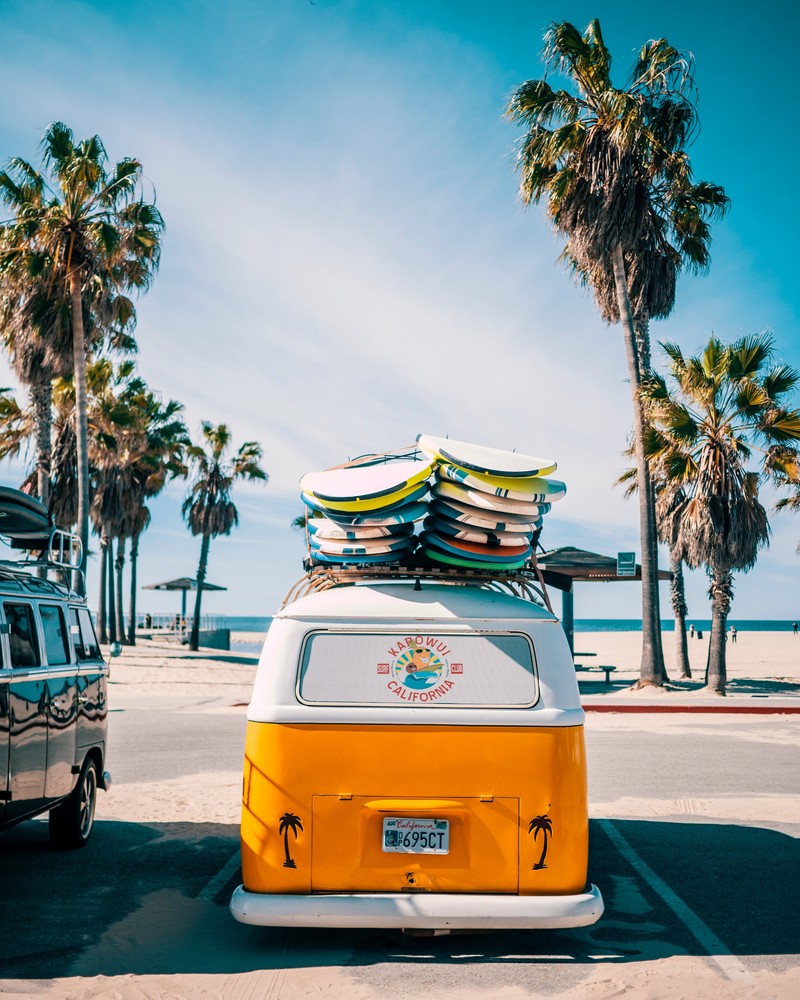 Yellow van with surfboards on top parked in front of a beach (california, cars, club, holiday, orange)