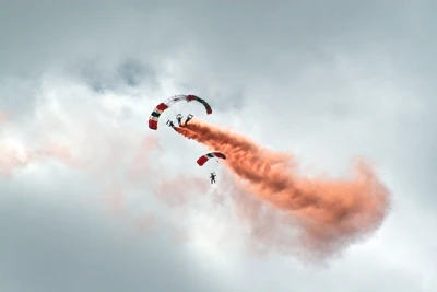 Paraquedistas realizando acrobacias com trilhas de fumaça coloridas no céu