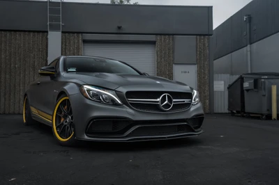 Sleek Mercedes-Benz E-Class avec des accents jaunes personnalisés et des jantes en alliage, garé dans un cadre industriel.