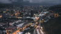 Aerial night view of a vibrant metropolitan cityscape with illuminated buildings and winding railway tracks.