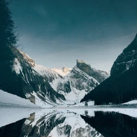 Montagnes enneigées se reflétant dans des eaux calmes au milieu d'un paysage naturel dramatique