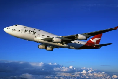 Qantas Boeing 747 парит в ясном голубом небе среди пушистых облаков.