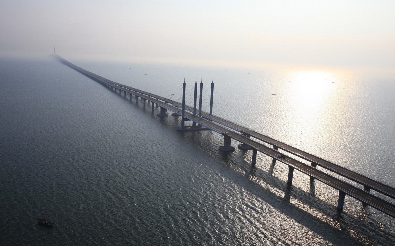 Arafed bridge over the water with a boat in the distance (bridge, cable stayed bridge, fog, sea, pier)