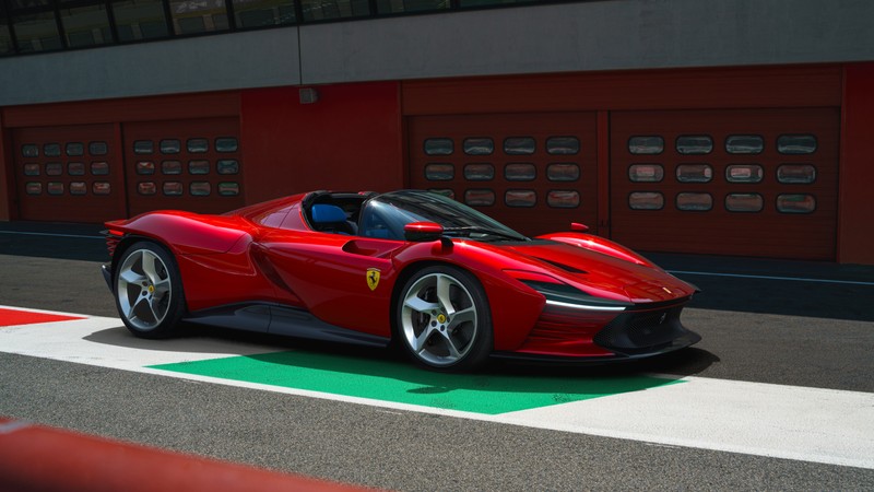 Красный спортивный автомобиль ferrari едет по трассе рядом с гаражем (феррари дейтона sp3, ferrari daytona sp3, спортивные автомобили, суперкары, гоночная трасса)