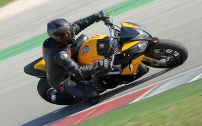 Piloto con equipo completo maniobrando una Aprilia Tuono en la pista durante una competencia de superbikes.