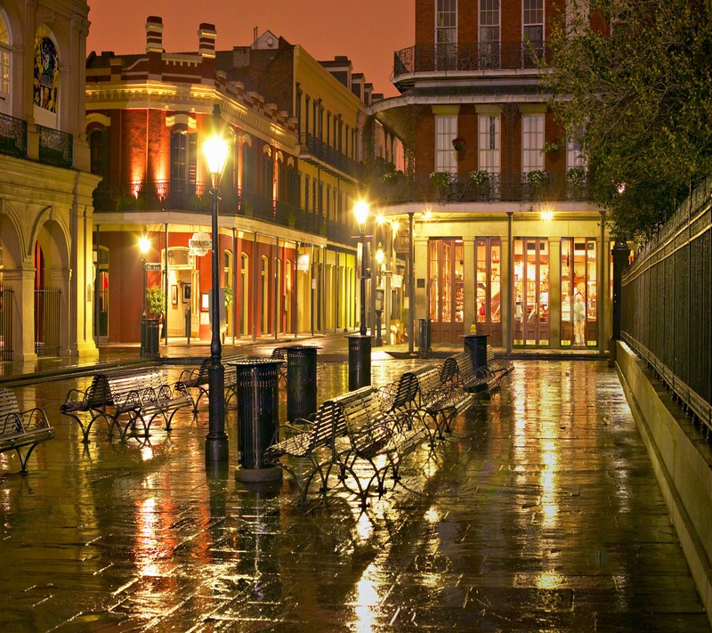 Il y a des bancs sur le trottoir sous la pluie la nuit (lumières de la ville, papier peint)