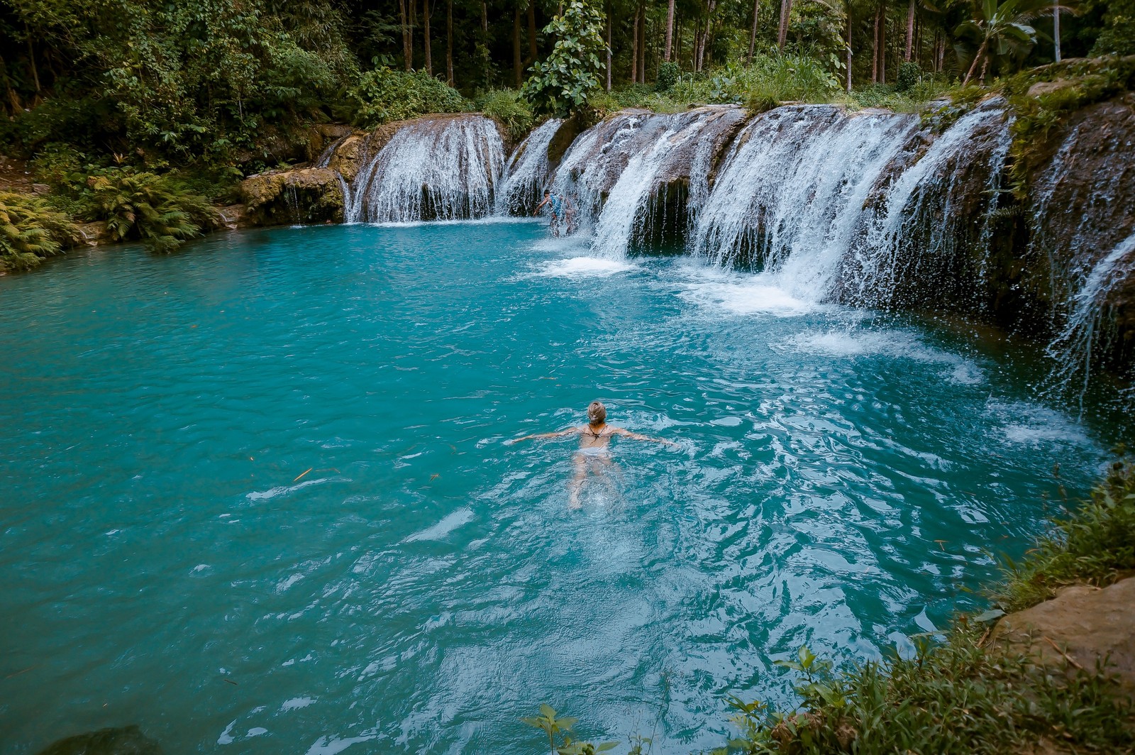 Um homem nadando em uma piscina perto de uma cachoeira (cachoeira, corpo de água, recursos hídricos, água, natureza)