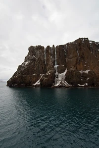 Cliff coberto de neve com vista para as serenas águas antárticas