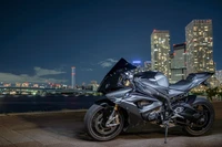 Motocicleta BMW S1000RR iluminada contra un horizonte urbano por la noche