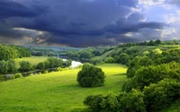 Prairie verdoyante et luxuriante dans les hautes terres sous un ciel dramatique, avec une rivière sinueuse et des arbres éparpillés.