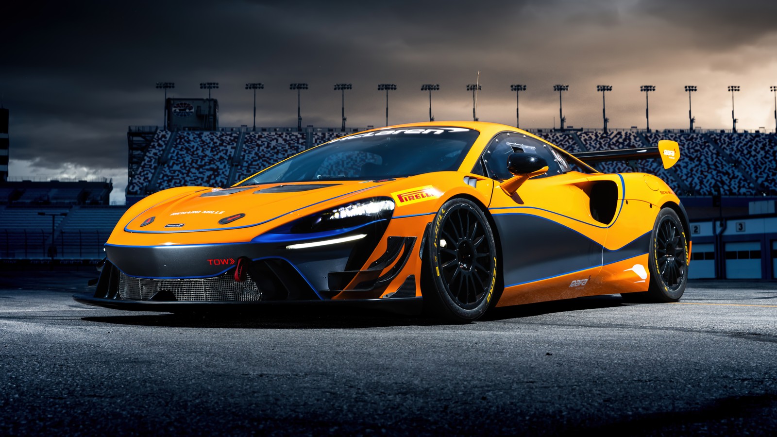 A yellow mclaren car parked in front of a stadium (mclaren artura gt4, 5k, race track, cars, 4k wallpaper)