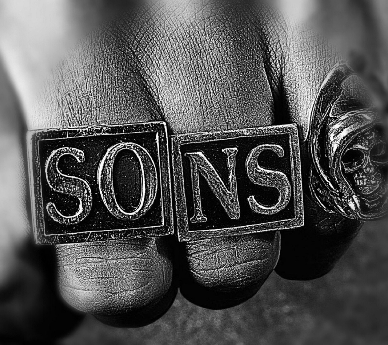 Un primer plano de la mano de una persona sosteniendo un anillo con la palabra "sons" (fx, motocicleta, espectáculo, soa, hijos)