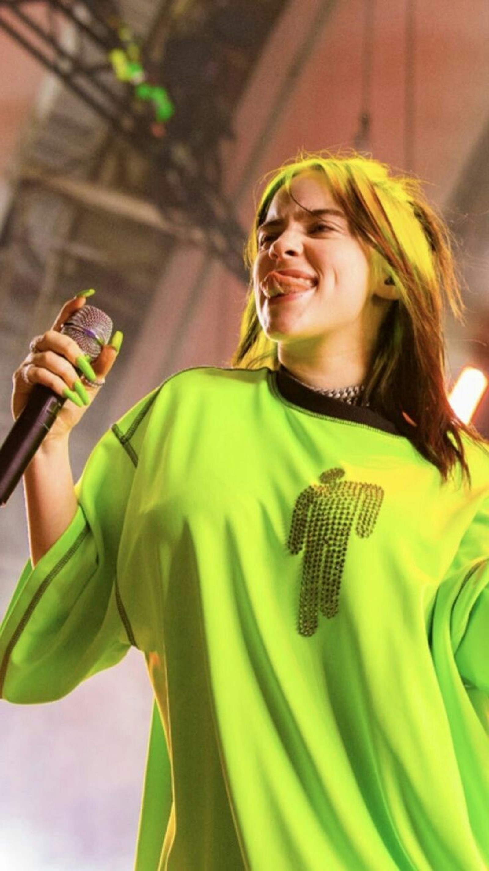 Araffe woman in a green shirt holding a microphone and smiling (billie, eilish)