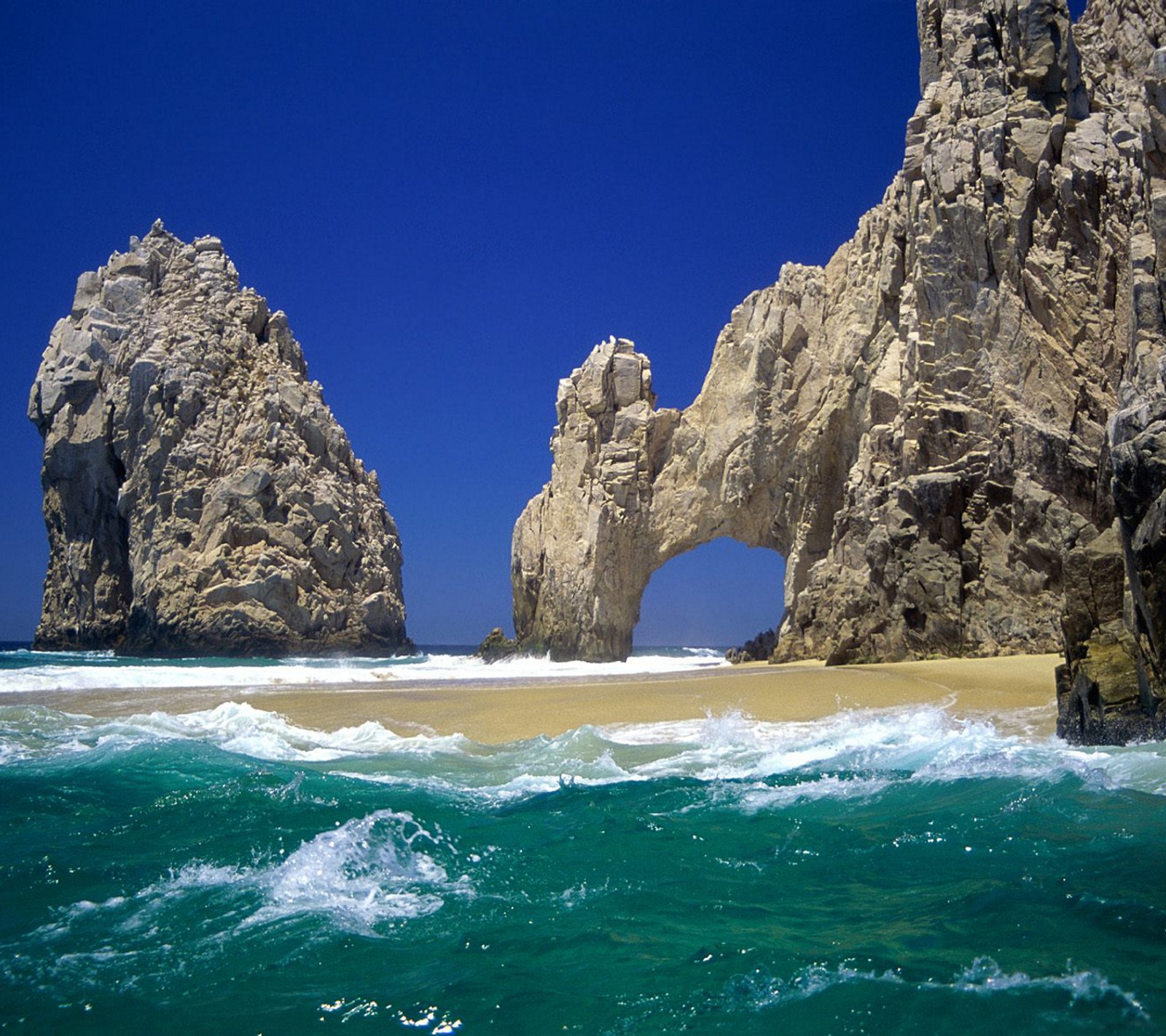 There are two large rocks in the water near the beach (beach, sand, sky, waves)