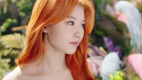 Minatozaki Sana do TWICE com cabelo laranja vibrante, capturada em um momento sereno em meio à vegetação exuberante.