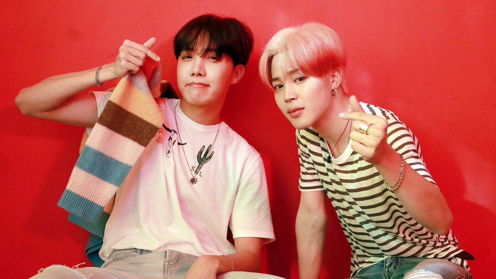 Two young men sitting next to each other on a red wall (j hope, jung ho seok, jimin, park ji min, bts)