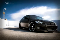 Élégante BMW Série 3 noire avec des jantes personnalisées capturée contre un ciel bleu clair.