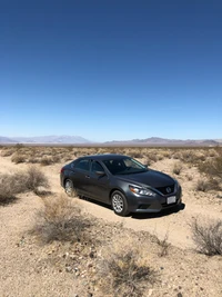 A sleek mid-size sedan parked on a rugged road in the Mojave Desert, surrounded by a sparse plant community and expansive landscape.