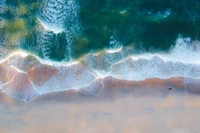 Vista aérea de serenas olas de playa que lamen la suave orilla de arena bajo vibrantes colores costeros.