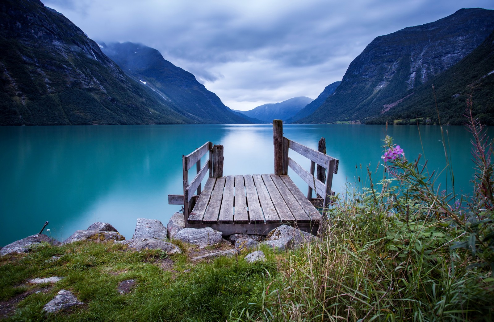 A wooden bridge over a lake with mountains in the background (fjord, lake, nature, mountain, highland)