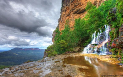 Cascada serena que cae entre colinas exuberantes y cielos dramáticos