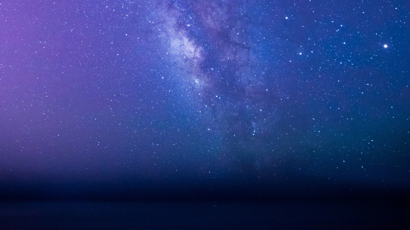 Um close de uma pessoa em pé na praia sob um céu cheio de estrelas (via láctea, astronomia, azul, atmosfera, roxo)