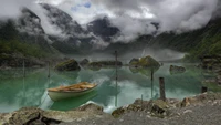 Lago sereno rodeado de montañas y niebla con un bote anclado cerca