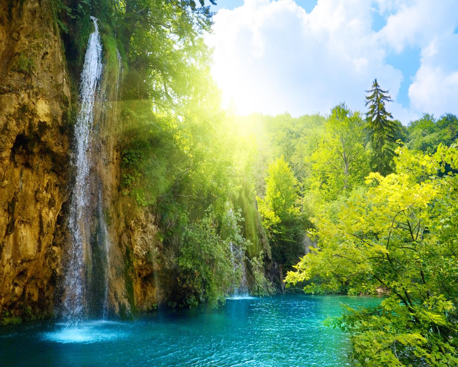 A waterfall in the middle of a forest with a blue pool (beam, lake, sun)