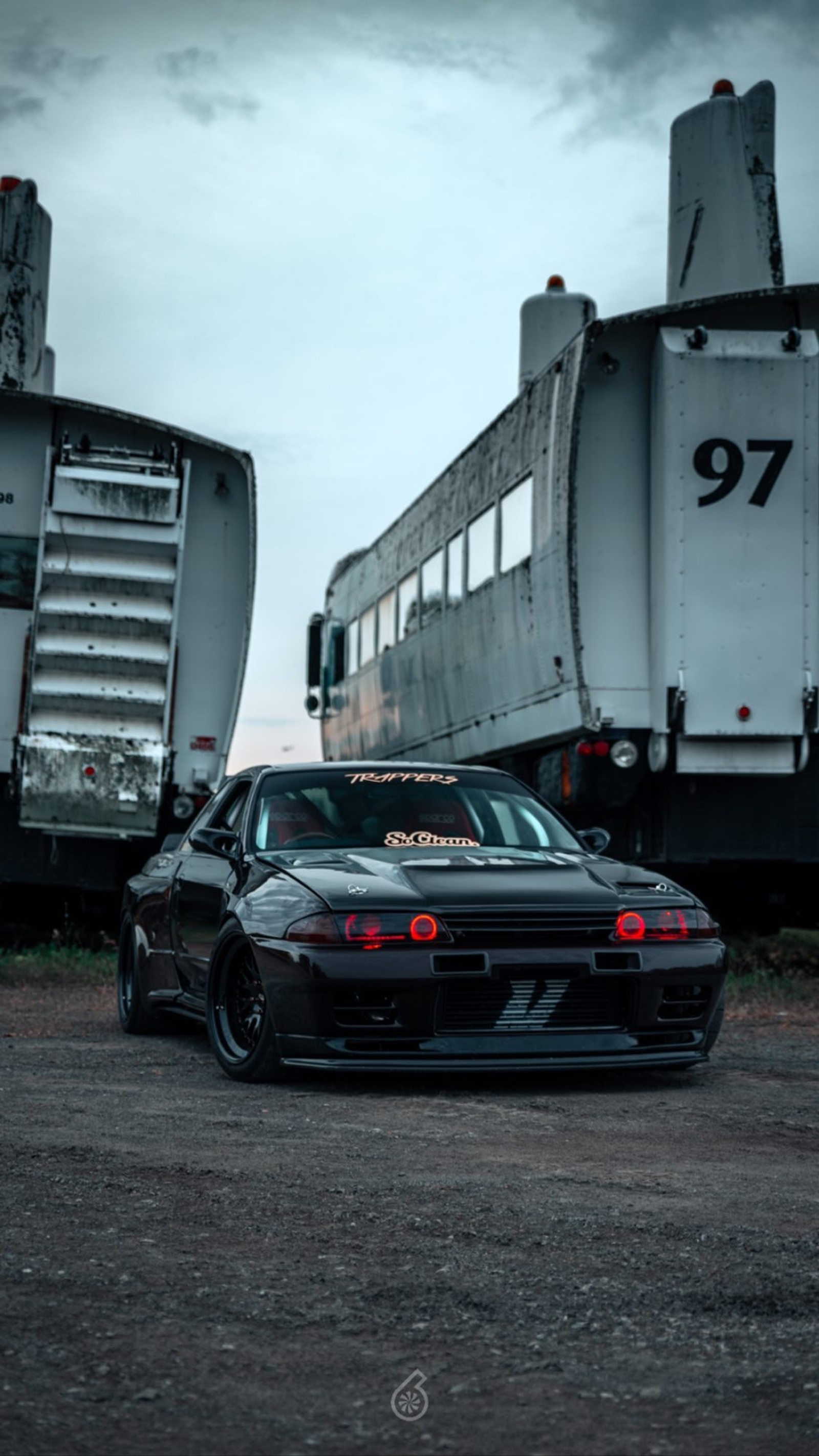 There is a black car parked next to a train on the tracks (jdm, r32, skyline, tuning)