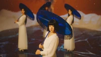 A captivating scene featuring a central figure in white attire holding a blue fringed umbrella, surrounded by three other similarly dressed figures, set against a warm, artistic backdrop.