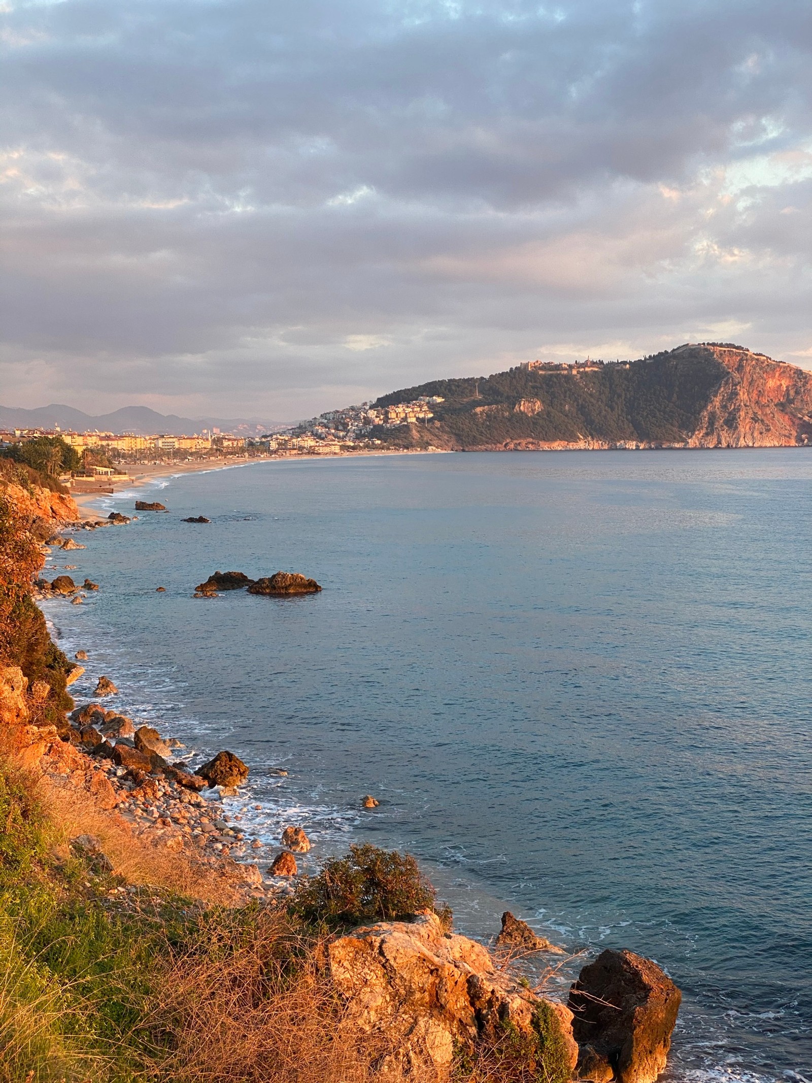 There is a view of a beach with a cliff and a body of water (sea, water, cloud, water resources, mountain)