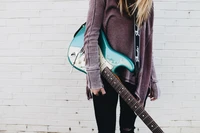 Músico elegante con guitarra eléctrica en turquesa contra una pared de ladrillo blanco