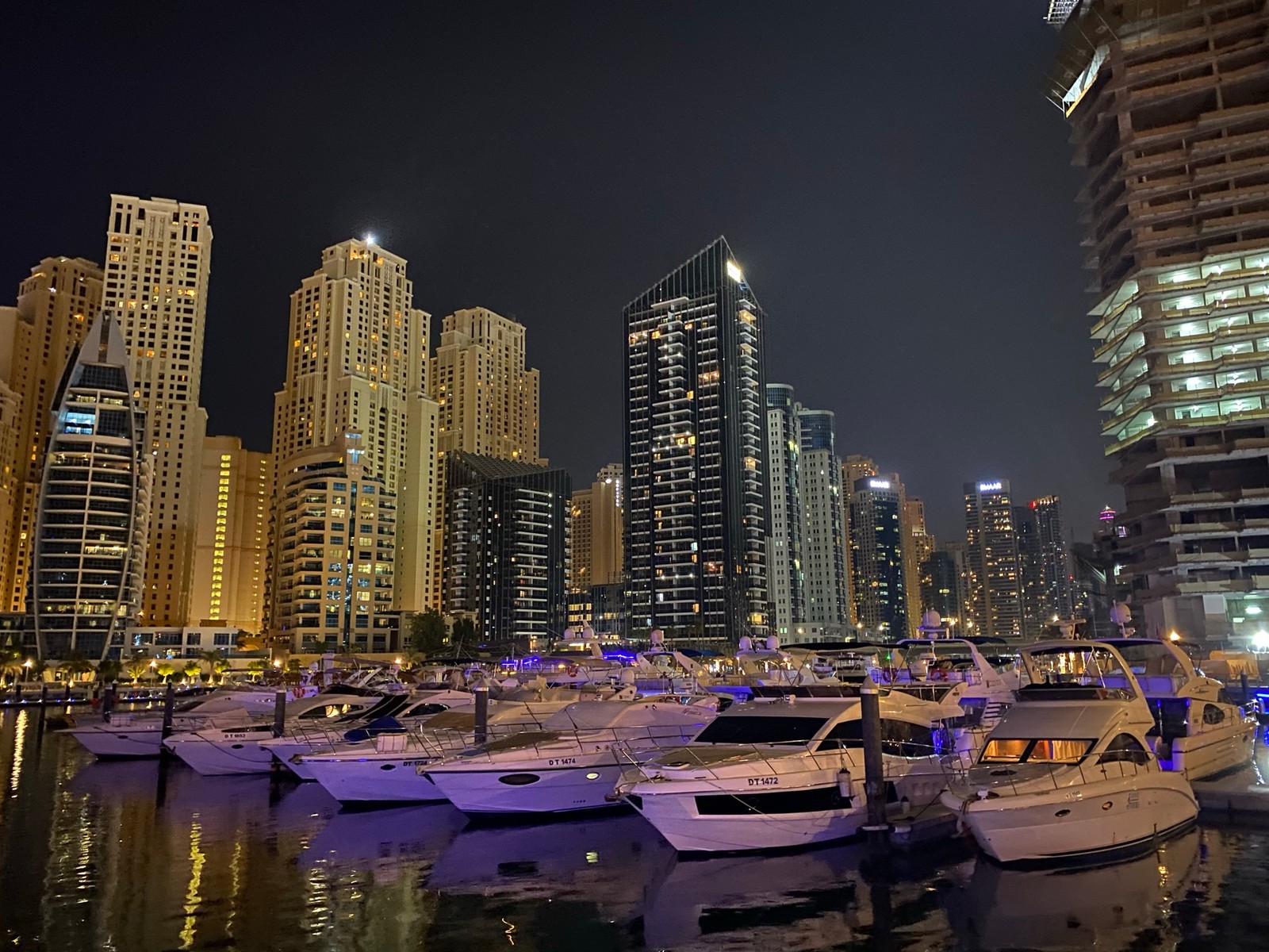 Los botes están atracados en el agua frente a una ciudad por la noche (dubái, dubai, marina de dubái, paisaje urbano, bloque de torre)