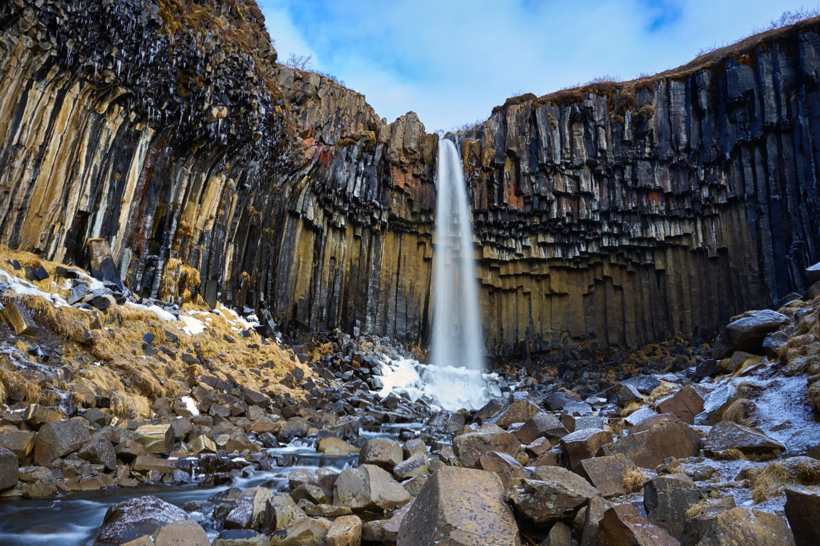 Uma cachoeira caindo de um penhasco rochoso em um rio (cachoeira svartifoss, parque nacional de vatnajökull, colunas de lava, rochas, islândia)