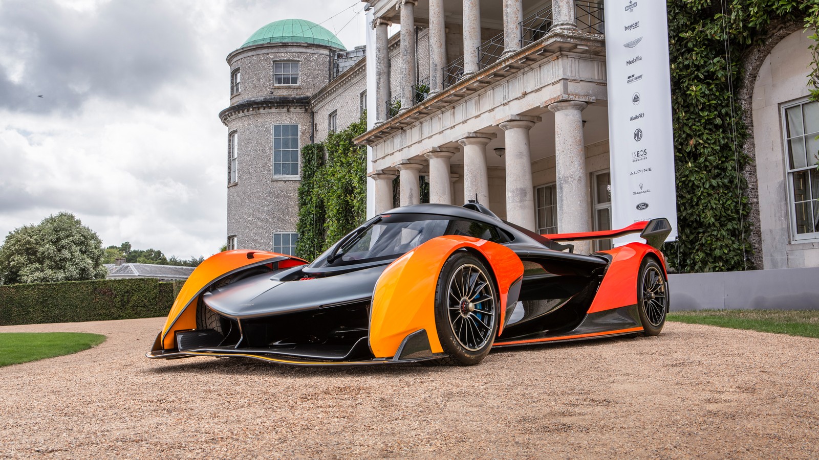 A close up of a black and orange race car parked in front of a building (mclaren solus gt, goodwood festival of speed, 2023, 5k, cars)